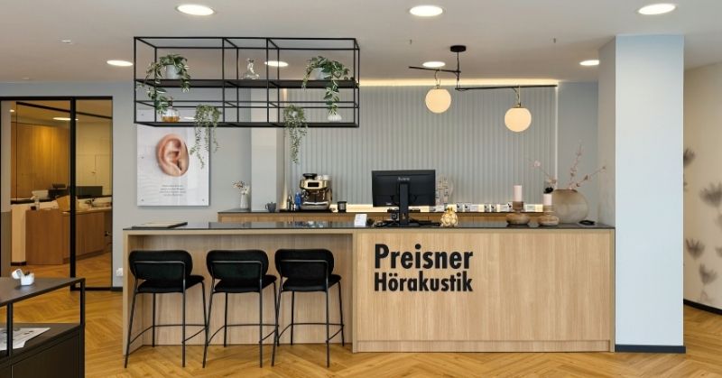 Empfangsbereich eines Hörakustik-Fachgeschäfts mit dem modularen CAROLINE Einrichtungssystem, individueller Empfangstheke und schwebendem Regalsystem.