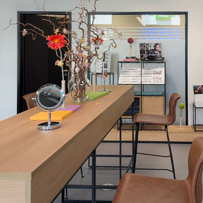 Consultation area in optical shop with long wooden table, mirrors and modular eyewear display.