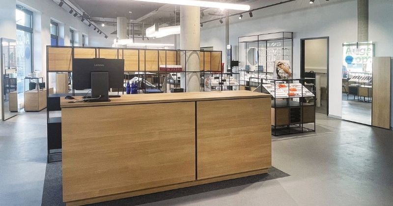 Modern optical shop reception area with wooden counter and modular furnishings in the background.