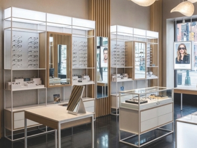Modernes Optikgeschäft mit modularen Wandpräsentationen, Spiegeln und zentraler Brillenvitrine.