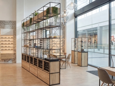 Modernes Optikgeschäft mit modularer Raumteiler-Präsentation, Pflanzen, Stauraum und Brillendisplays.