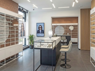 Modernes Optikgeschäft mit Wandpräsentationen, Mittelraumvitrine, Beratungssitzplatz und integrierten Spiegeln.