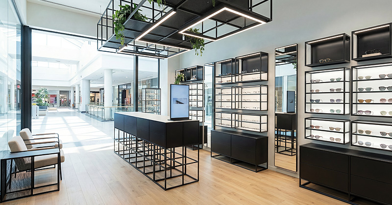 Modernes Optikgeschäft mit beleuchteten Brillenpräsentationen, Spiegeln, Stauraum und begrünten Deckenelementen.