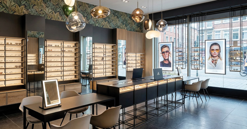 Elegantes Optikgeschäft mit beleuchteten Wandpräsentationen, Beratungstischen und moderner Schaufenstergestaltung.