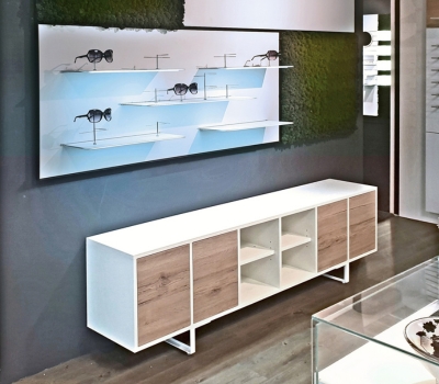 Modulare Wandpräsentation für Brillen mit weißen Ablagen und passendem Sideboard.